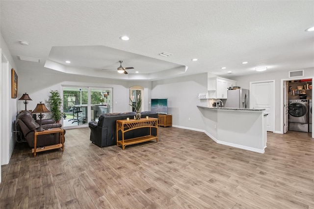 14509 Mayer Ave, Hudson, FL 34669 - living room featuring a raised ceiling, light wood finished floors, a textured ceiling, a ceiling fan, and separate washer and dryer