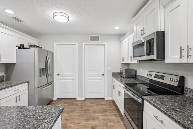 14509 Mayer Ave, Hudson, FL 34669 - kitchen with stainless steel appliances, white cabinets, light wood-style flooring, recessed lighting, and dark stone counters