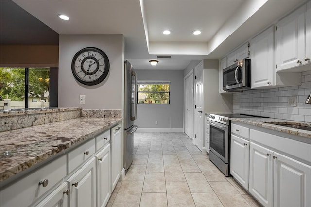 200 Gretchen Ct, Oldsmar, FL 34677 - kitchen with stainless steel appliances, light stone countertops, a raised ceiling, decorative backsplash, and white cabinetry