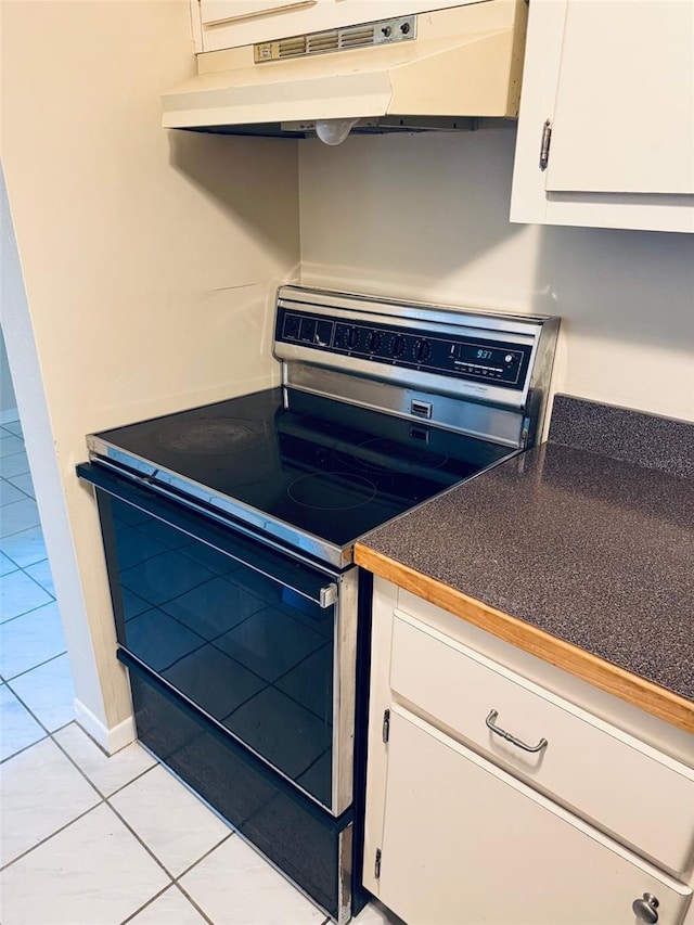 2525 W Bay Dr Unit A33, Largo, FL 33770 - kitchen with stainless steel range with electric cooktop, under cabinet range hood, light tile patterned flooring, white cabinets, and dark countertops