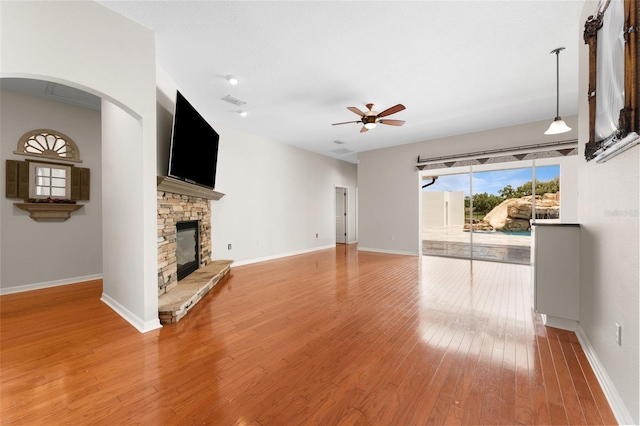 2702 Rogers Ranch Rd, Lithia, FL 33547 - unfurnished living room featuring a ceiling fan, a stone fireplace, light wood finished floors, and arched walkways
