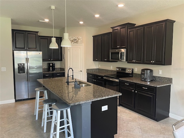 1596 Ludington Ave, Wesley Chapel, FL 33543 - kitchen featuring appliances with stainless steel finishes, a center island with sink, a kitchen bar, dark stone countertops, and a textured ceiling