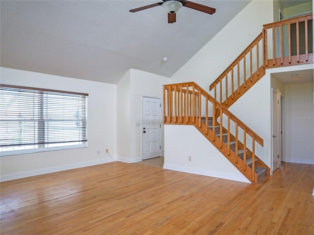 8759 Orient Way NE, Saint Petersburg, FL 33702 - unfurnished living room with a ceiling fan, stairs, light wood-style flooring, high vaulted ceiling, and a textured ceiling