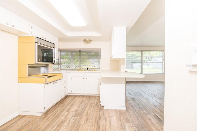 3406 Rock Royal Dr, Holiday, FL 34691 - kitchen featuring a peninsula, light countertops, stainless steel microwave, light wood-style floors, and white cabinetry