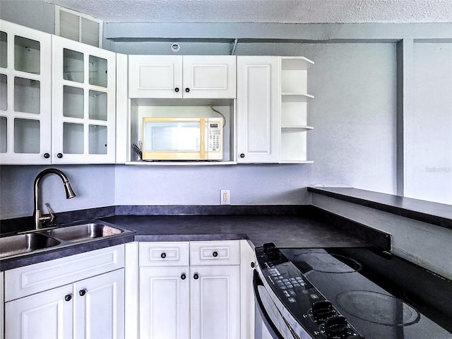 3315 58th Ave S Unit 409, Saint Petersburg, FL 33712 - kitchen with white microwave, range with electric stovetop, dark countertops, white cabinetry, and glass insert cabinets