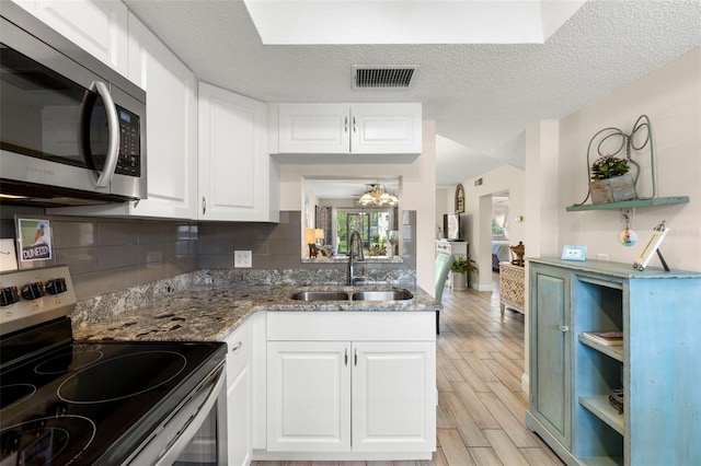 1370 Heather Ridge Blvd Unit 105, Dunedin, FL 34698 - kitchen featuring appliances with stainless steel finishes, open shelves, light wood-style flooring, white cabinetry, and a textured ceiling