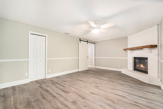 4117 Daventry Ln, Palm Harbor, FL 34685 - unfurnished living room with a barn door, wood finished floors, ceiling fan, a textured ceiling, and a brick fireplace