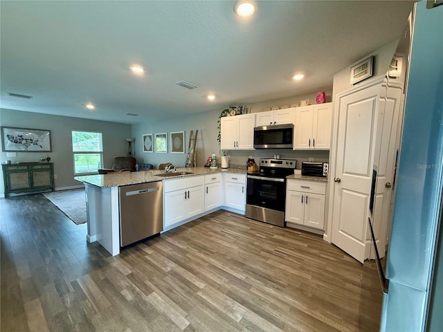 6270 Airmont Dr, Spring Hill, FL 34606 - kitchen with stainless steel appliances, open floor plan, a peninsula, white cabinets, and wood finished floors