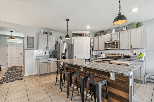 33678 Jasper Stone Dr, Wesley Chapel, FL 33543 - kitchen with appliances with stainless steel finishes, tasteful backsplash, light tile patterned floors, arched walkways, and light stone counters