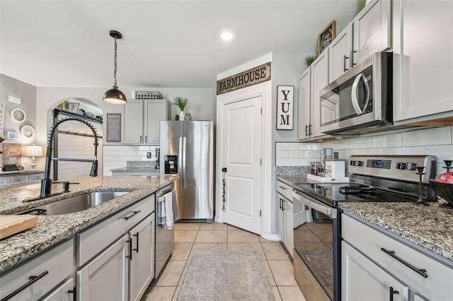 33678 Jasper Stone Dr, Wesley Chapel, FL 33543 - kitchen with stainless steel appliances, backsplash, light tile patterned flooring, hanging light fixtures, and light stone countertops