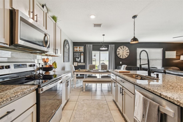 33678 Jasper Stone Dr, Wesley Chapel, FL 33543 - kitchen with stainless steel appliances, open floor plan, light stone countertops, decorative light fixtures, and light tile patterned flooring