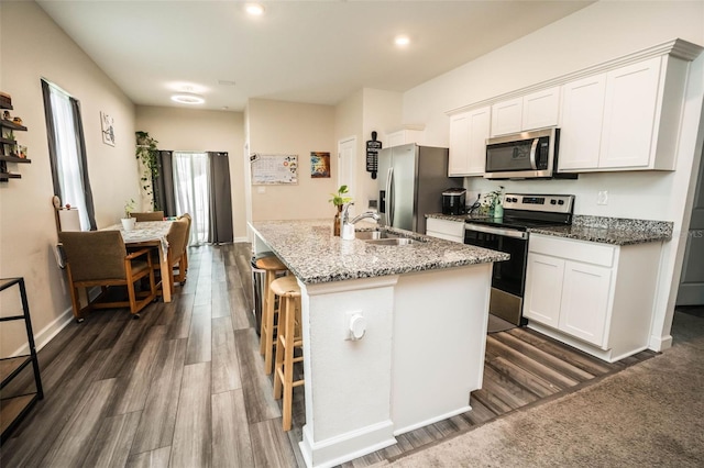 35210 Daisy Meadow Loop, Zephyrhills, FL 33541 - kitchen featuring stainless steel appliances, dark wood-style flooring, white cabinets, a breakfast bar area, and an island with sink
