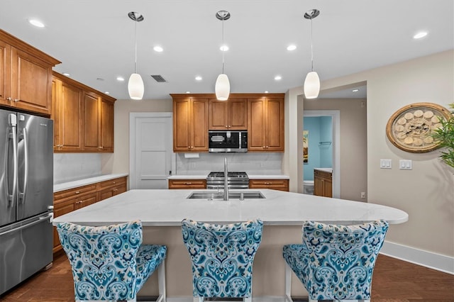 200 Main St Unit 204, Dunedin, FL 34698 - kitchen featuring appliances with stainless steel finishes, brown cabinets, recessed lighting, decorative backsplash, and a kitchen island with sink