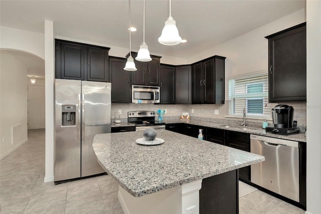 11240 Merganser Way, New Port Richey, FL 34654 - kitchen featuring appliances with stainless steel finishes, arched walkways, light stone counters, backsplash, and a center island