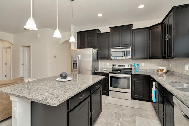 11240 Merganser Way, New Port Richey, FL 34654 - kitchen with stainless steel appliances, arched walkways, light stone counters, a center island, and decorative light fixtures