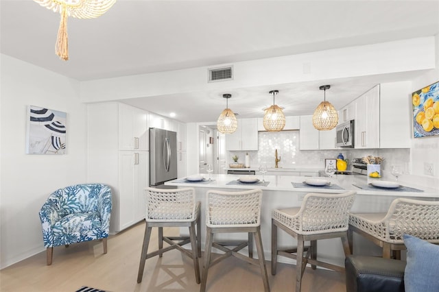 10280 Gulf Blvd Unit 12, Treasure Island, FL 33706 - kitchen with appliances with stainless steel finishes, a peninsula, decorative backsplash, a kitchen breakfast bar, and light wood-style flooring