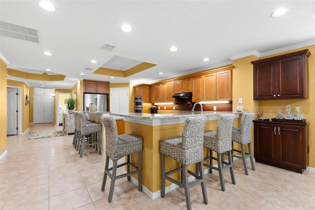 3805 Gulf Blvd Unit 401, St Pete Beach, FL 33706 - kitchen with appliances with stainless steel finishes, ornamental molding, a tray ceiling, a peninsula, and a kitchen bar