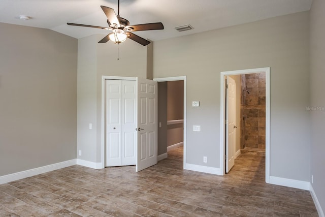 3298 Covered Bridge Dr W, Dunedin, FL 34698 - unfurnished bedroom with wood finished floors, a closet, high vaulted ceiling, ensuite bathroom, and a ceiling fan