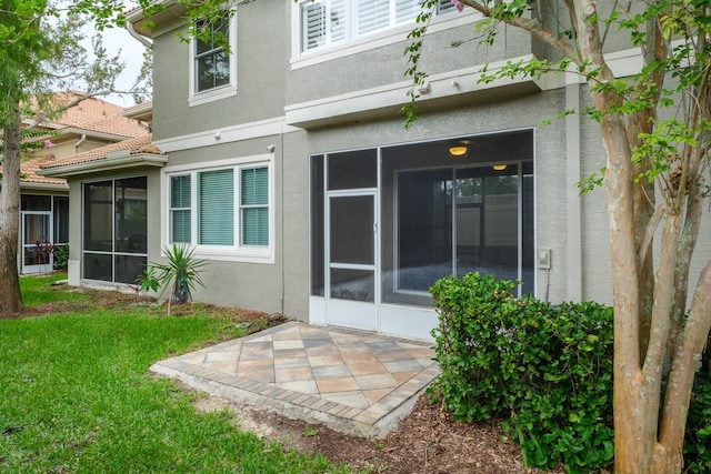 3298 Covered Bridge Dr W, Dunedin, FL 34698 - rear view of house with a sunroom, stucco siding, a patio area, and a yard