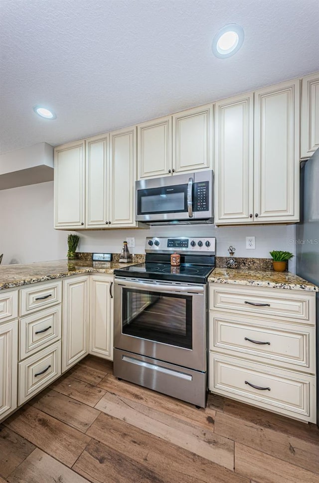 5157 Silent Loop Unit 301, New Port Richey, FL 34652 - kitchen with appliances with stainless steel finishes, cream cabinets, wood-type flooring, light stone counters, and recessed lighting