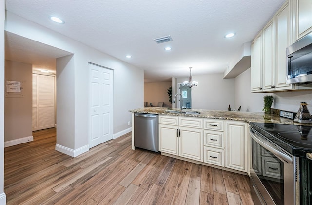 5157 Silent Loop Unit 301, New Port Richey, FL 34652 - kitchen featuring appliances with stainless steel finishes, a peninsula, a chandelier, light wood-style flooring, and light stone countertops