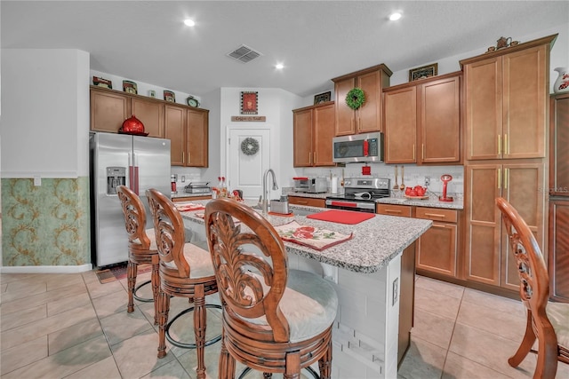 289 Siesta Vista Ct, Davenport, FL 33896 - kitchen with stainless steel appliances, brown cabinets, a kitchen island with sink, a breakfast bar, and light stone counters