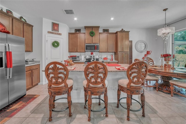 289 Siesta Vista Ct, Davenport, FL 33896 - kitchen with appliances with stainless steel finishes, brown cabinets, light stone countertops, a center island with sink, and recessed lighting