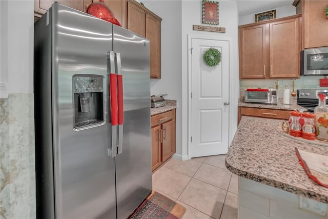 289 Siesta Vista Ct, Davenport, FL 33896 - kitchen featuring stainless steel appliances, brown cabinets, light stone counters, light tile patterned flooring, and backsplash