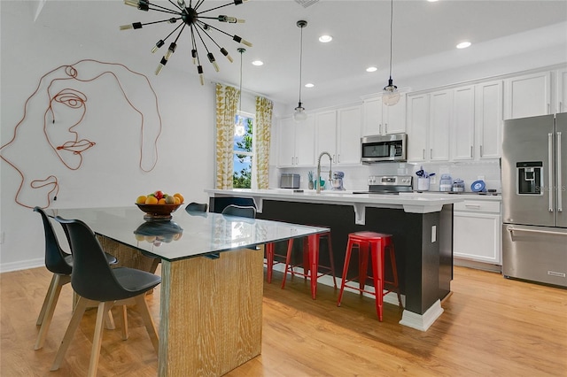 356 Irving Bend Dr, Groveland, FL 34736 - kitchen with appliances with stainless steel finishes, a kitchen bar, a center island with sink, light wood-style flooring, and light countertops