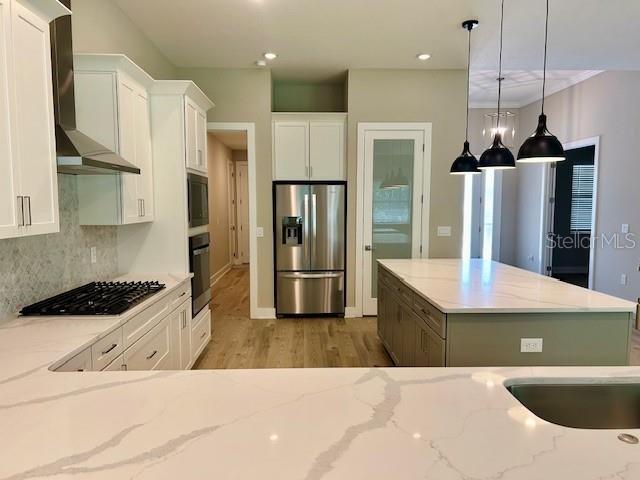 4800 Hickory Oak Dr, Brooksville, FL 34601 - kitchen with black appliances, wall chimney range hood, white cabinets, light wood-style floors, and light stone counters