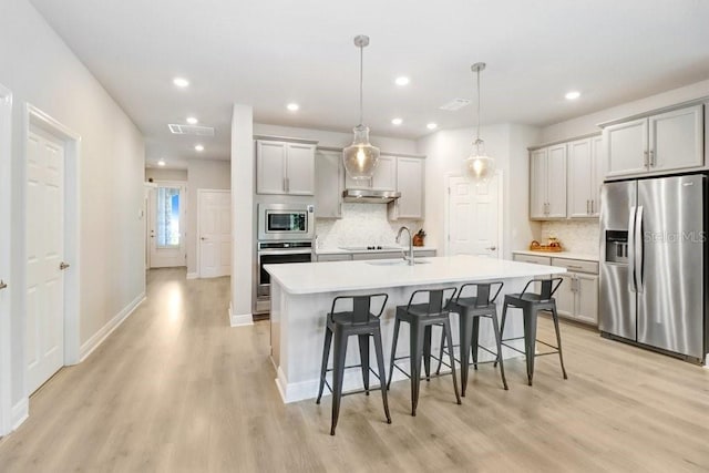 11809 Catawba Cv, Parrish, FL 34219 - kitchen featuring appliances with stainless steel finishes, light wood-style flooring, a kitchen breakfast bar, decorative backsplash, and an island with sink