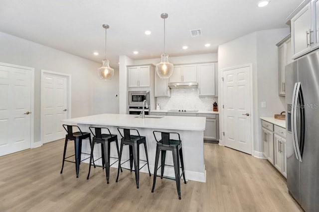 11809 Catawba Cv, Parrish, FL 34219 - kitchen featuring appliances with stainless steel finishes, light wood finished floors, under cabinet range hood, a breakfast bar, and recessed lighting