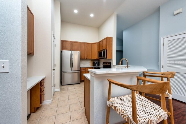 7001 Interbay Blvd Unit 121, Tampa, FL 33616 - kitchen featuring appliances with stainless steel finishes, a peninsula, decorative backsplash, brown cabinets, and light countertops