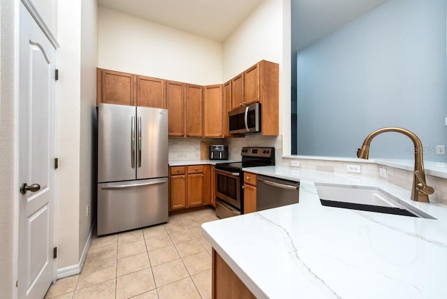 7001 Interbay Blvd Unit 121, Tampa, FL 33616 - kitchen featuring stainless steel appliances, brown cabinets, backsplash, light tile patterned flooring, and light stone counters