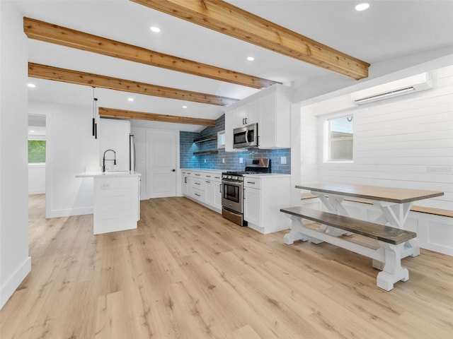 960 65th St S, Saint Petersburg, FL 33707 - kitchen featuring appliances with stainless steel finishes, a wall mounted air conditioner, light countertops, white cabinets, and decorative backsplash