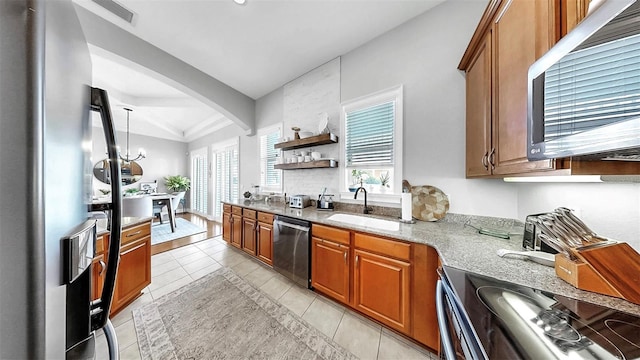 6545 Simone Shores Cir, Apollo Beach, FL 33572 - kitchen with stainless steel appliances, brown cabinetry, light stone counters, light tile patterned flooring, and arched walkways