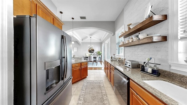 6545 Simone Shores Cir, Apollo Beach, FL 33572 - kitchen featuring stainless steel appliances, brown cabinetry, arched walkways, light stone countertops, and beam ceiling