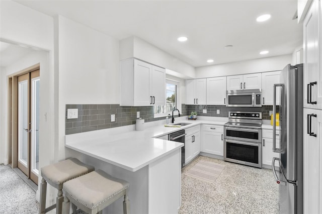 7950 Causeway Blvd N, Saint Petersburg, FL 33707 - kitchen featuring appliances with stainless steel finishes, a peninsula, white cabinets, dark speckled floor, and recessed lighting