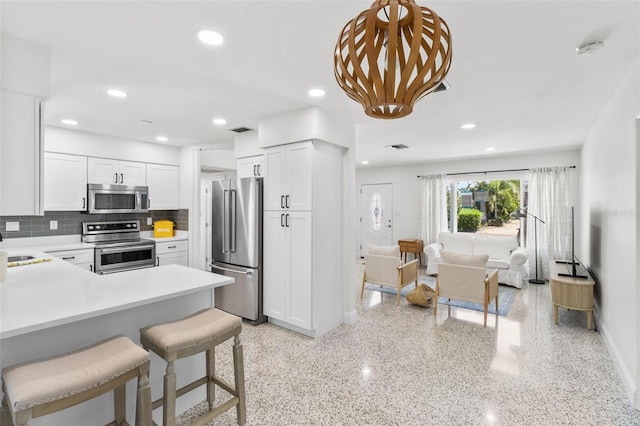 7950 Causeway Blvd N, Saint Petersburg, FL 33707 - kitchen featuring stainless steel appliances, backsplash, light countertops, a breakfast bar, and white cabinets
