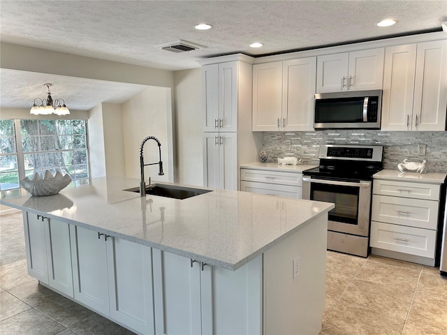 17017 Paula Ln, Lutz, FL 33558 - kitchen with stainless steel appliances, a textured ceiling, decorative backsplash, a center island with sink, and a chandelier