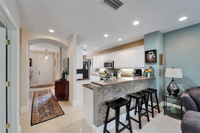 5642 Simonton St, Bradenton, FL 34203 - kitchen with appliances with stainless steel finishes, arched walkways, a breakfast bar area, white cabinetry, and backsplash