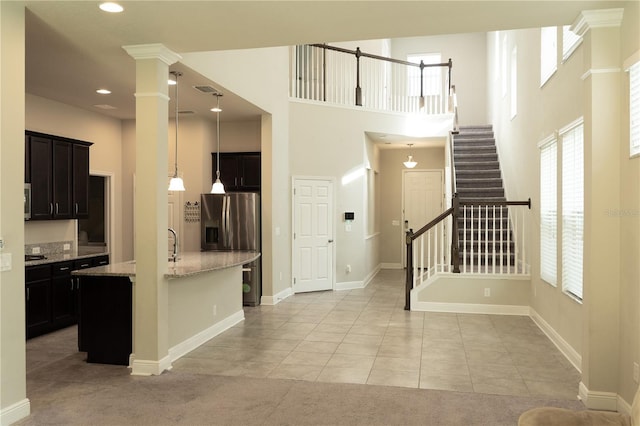 7508 Sea Lilly Ct, Apollo Beach, FL 33572 - kitchen with light stone countertops, stainless steel refrigerator with ice dispenser, light tile patterned floors, a high ceiling, and hanging light fixtures