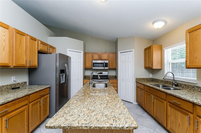 13190 Drysdale St, Spring Hill, FL 34609 - kitchen with stainless steel appliances, a kitchen island with sink, light tile patterned floors, light stone counters, and brown cabinetry