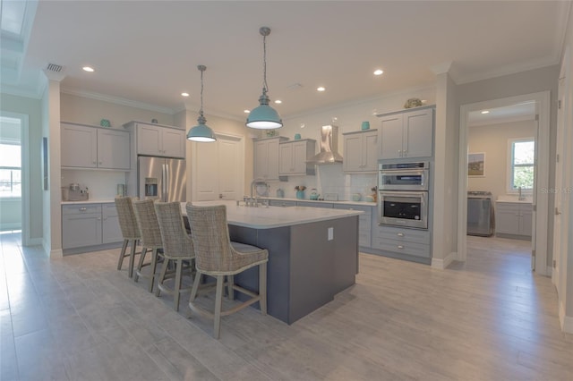 9016 Falcon Ct, Venice, FL 34293 - kitchen with gray cabinets, wall chimney range hood, stainless steel appliances, washer / dryer, and light countertops