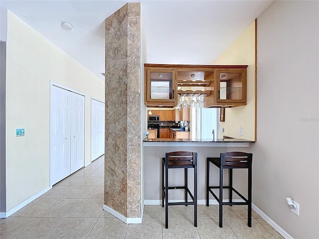 4222 Trumpworth Ct, Valrico, FL 33596 - kitchen featuring a kitchen bar, glass insert cabinets, light tile patterned flooring, brown cabinets, and stainless steel microwave