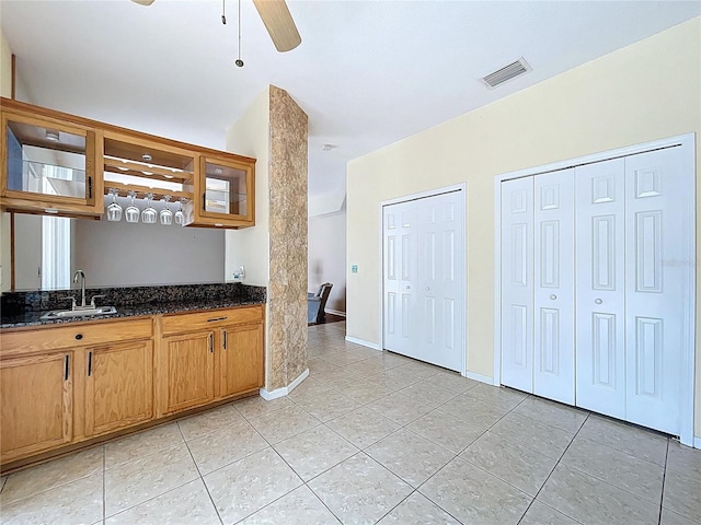 4222 Trumpworth Ct, Valrico, FL 33596 - kitchen with light tile patterned floors, glass insert cabinets, a ceiling fan, brown cabinets, and dark stone counters