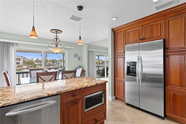131 N Tessier Dr, St Pete Beach, FL 33706 - kitchen featuring appliances with stainless steel finishes, decorative light fixtures, brown cabinets, light stone counters, and a textured ceiling