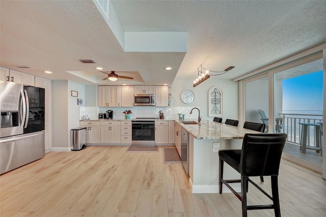17408 Gulf Blvd Unit 601, Redington Shores, FL 33708 - kitchen with appliances with stainless steel finishes, a peninsula, a textured ceiling, decorative backsplash, and light wood-style flooring