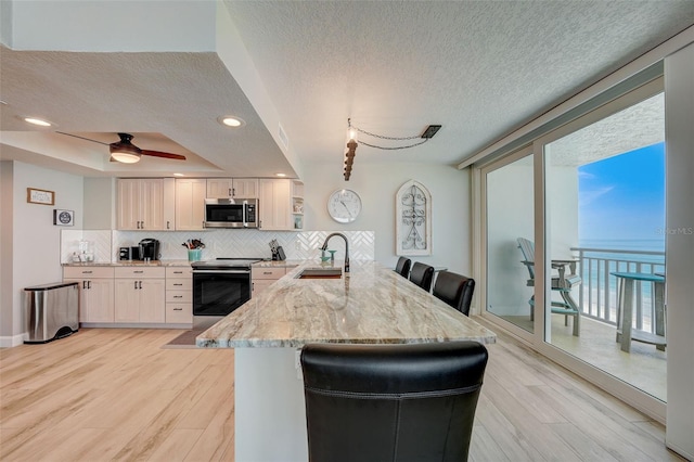 17408 Gulf Blvd Unit 601, Redington Shores, FL 33708 - kitchen featuring appliances with stainless steel finishes, a peninsula, a textured ceiling, backsplash, and light stone countertops