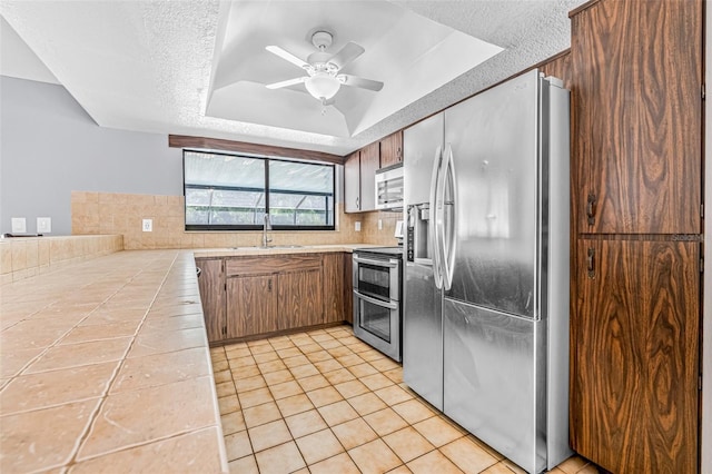 10430 Bobcat Dr, New Port Richey, FL 34654 - kitchen featuring stainless steel appliances, tile countertops, a tray ceiling, tasteful backsplash, and a ceiling fan